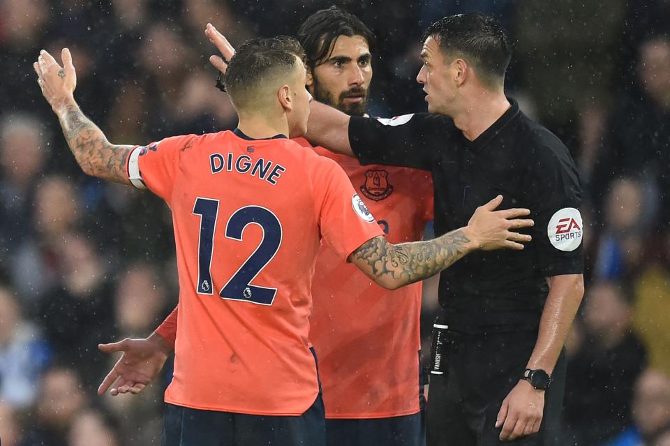 Referee Andy Madley (R) waves away the protests of Everton's French defender Lucas Digne (L) and Everton's Portuguese midfielder André Gomes (C) after he awarded a penalty to Brighton following a review by the Video Assistant Referee (VAR) during the English Premier League football match between Brighton and Hove Albion and Everton at the American Express Community Stadium in Brighton, southern England on October 26, 2019. (Photo by Glyn KIRK / AFP) / RESTRICTED TO EDITORIAL USE. No use with unauthorized audio, video, data, fixture lists, club/league logos or 'live' services. Online in-match use limited to 120 images. An additional 40 images may be used in extra time. No video emulation. Social media in-match use limited to 120 images. An additional 40 images may be used in extra time. No use in betting publications, games or single club/league/player publications. /  (Photo by GLYN KIRK/AFP via Getty Images)