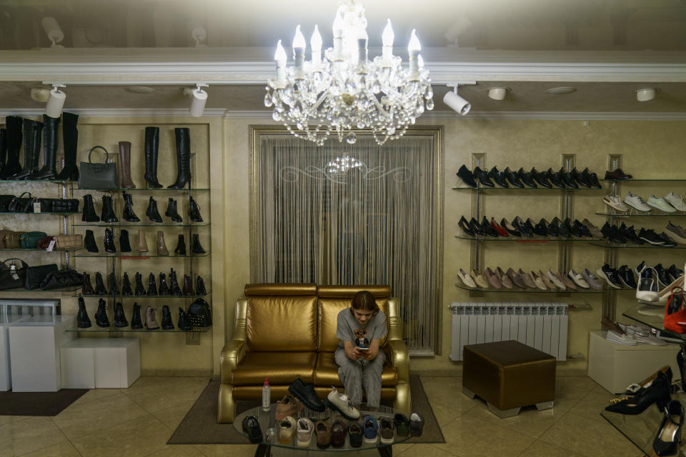 Sofia Mariia Bondar, 16, looks at her phone while sitting in the clothing shop where her mother works in Kramatorsk, Donetsk region, eastern Ukraine, Wednesday, Aug. 3, 2022. A piano player and singer who wants to study art at university after she finishes her final year of high school, Sofia Mariia said she was often bored since all her friends have left. Her mother, Viktoriia, said that with the danger of shelling always present and soldiers plying the streets, her daughter is no longer allowed to go out alone, and spends most of her time by her side. (AP Photo/David Goldman)