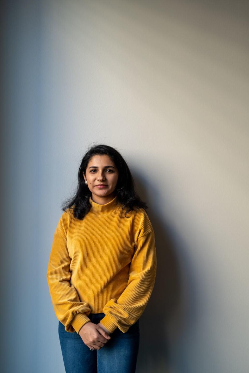 woman in a yellow shirt stands in front of a white wall