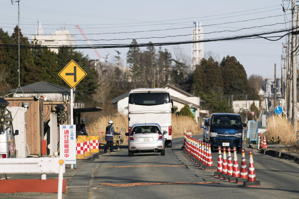 A security guard stops vehicles at a security checkpoint as they enter an area that requires a special permit to enter in Okuma town, Fukushima prefecture, northeastern Japan, Thursday, Feb. 25, 2021. Part of the buildings at the Fukushima Daiichi nuclear power plant is seen in the background. (AP Photo/Hiro Komae)