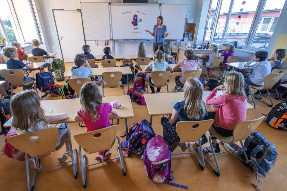 Teacher Francie Keller welcomes the pupils of class 3c in her classroom in the Lankow primary school to the first school day after the summer holidays in Schwerin, Germany, Monday, Aug. 3, 2020. In Mecklenburg-Western Pomerania, lessons will start again under corona conditions. The state ministers of education have agreed that the schools will return to regular operation after the holidays despite the Corona pandemic. (Jens Buettner/dpa via AP)