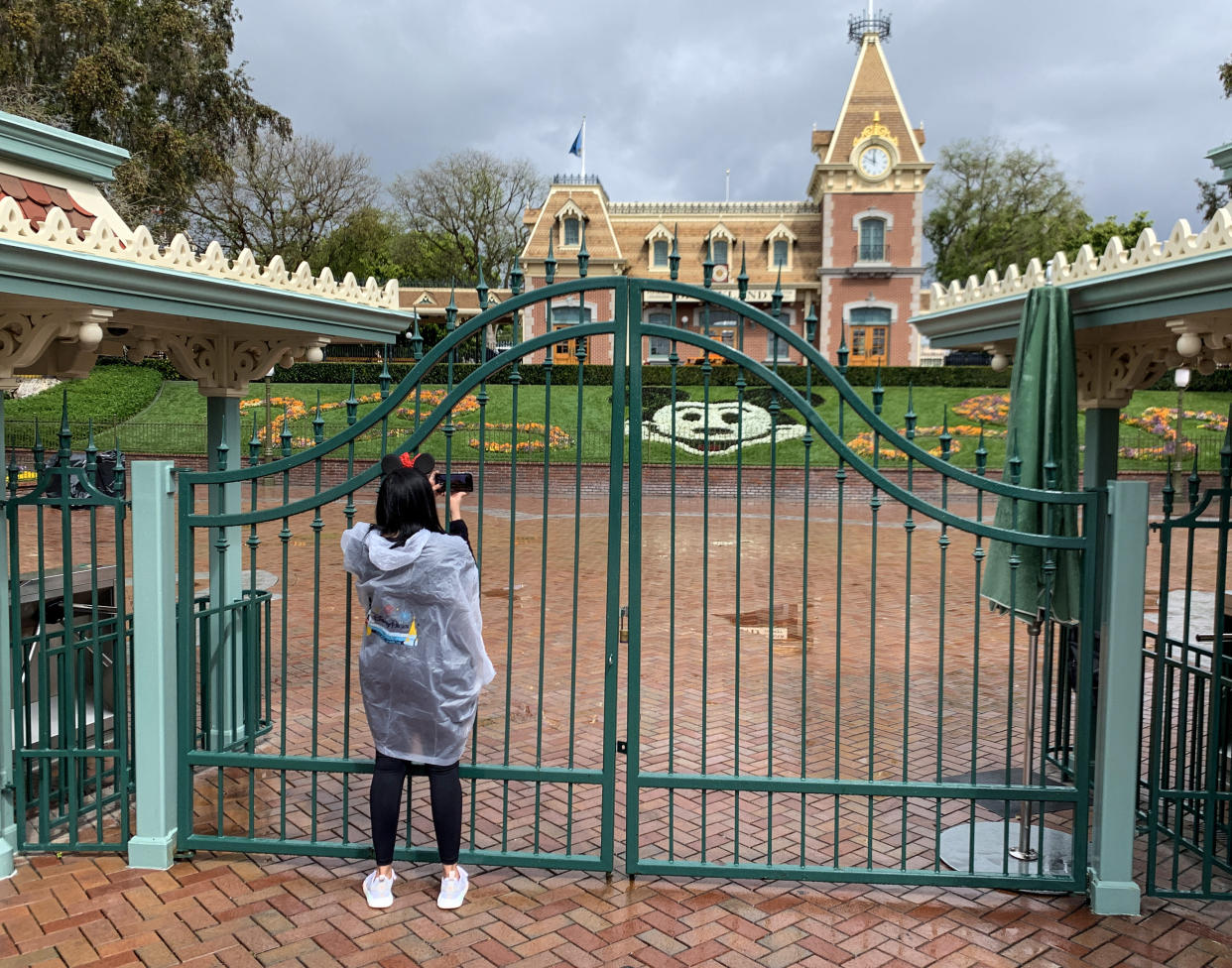 ANAHEIM, CA - MARCH 16: Disney will lay off 28,000 employees at Disneyland and Walt Disney World as the company continues to struggle with the impacts of the COVID-19 pandemic and the six-month closure of its Anaheim theme parks, the company announced today. A visitor to the Disneyland Resort takes a picture through a locked gate at the entrance to Disneyland in Anaheim, CA, on Monday, Mar 16, 2020. The entire Disneyland Resort is shut down due to the coronavirus (COVID-19) outbreak. (Photo by Jeff Gritchen/MediaNews Group/Orange County Register via Getty Images)