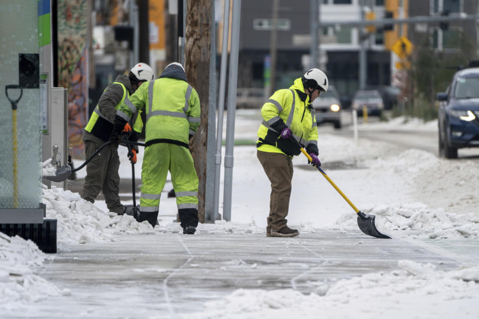 Workers clear snow along 82nd Ave., in Portland, Ore., Sunday, Jan. 14, 2024, a day after a winter storm hit the city with powerful winds, snow, sleet, and temperatures well below 20 degrees. (Mark Graves/The Oregonian via AP)