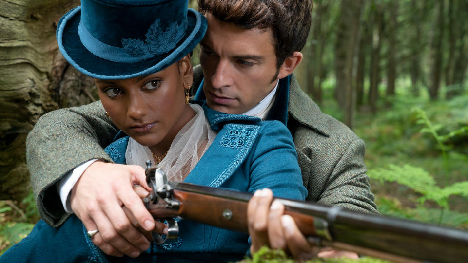 Kate Sharma (Simone Ashley) and Anthony Bridgerton (Jonathan Bailey) embrace as Anthony teaches Kate how to use a rifle.