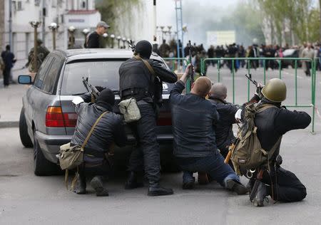 Pro-Russian armed men take cover behind a car near the local police headquarters in Luhansk, eastern Ukraine, April 29, 2014. REUTERS/Vasily Fedosenko