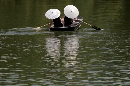 People protect themselves from the sun with parasols while rowing in Central Park as a heatwave continues to affect the region in New York