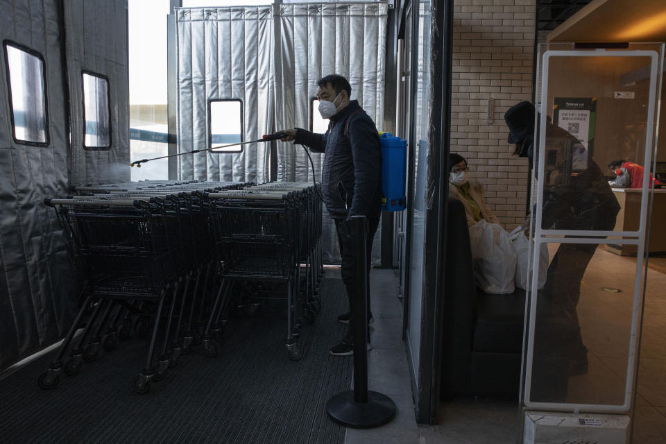 In this Tuesday, Feb. 18, 2020, photo, a staff at the 7Fresh supermarket disinfects the shopping trolleys in Beijing. Stores that offer online purchases are enjoying brisk sales as residents avoid going out during the current viral outbreak with authorities last week requiring people returning to the capital to self-quarantine at home or in a concentrated area for medical observation.(AP Photo/Ng Han Guan)