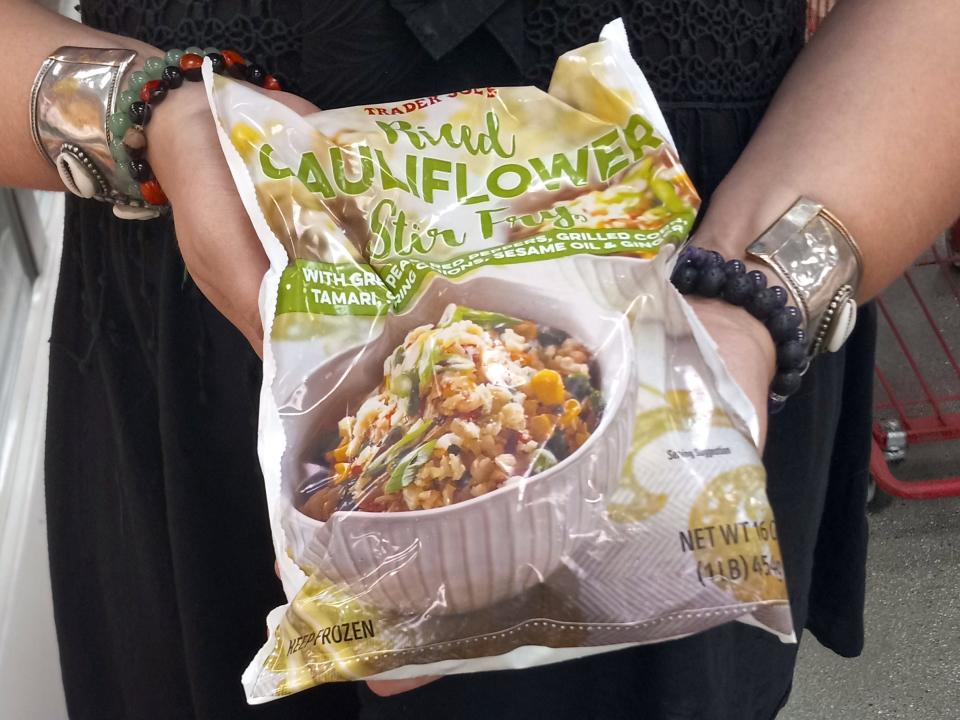 hands holding bag of frozen cauliflower fried rice in the freezer aisle of trader joes