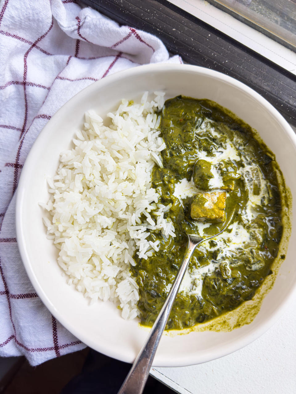 white bowl filled with half steamed rice and half a spinach-heavy curry with tofu, with a spoon inside