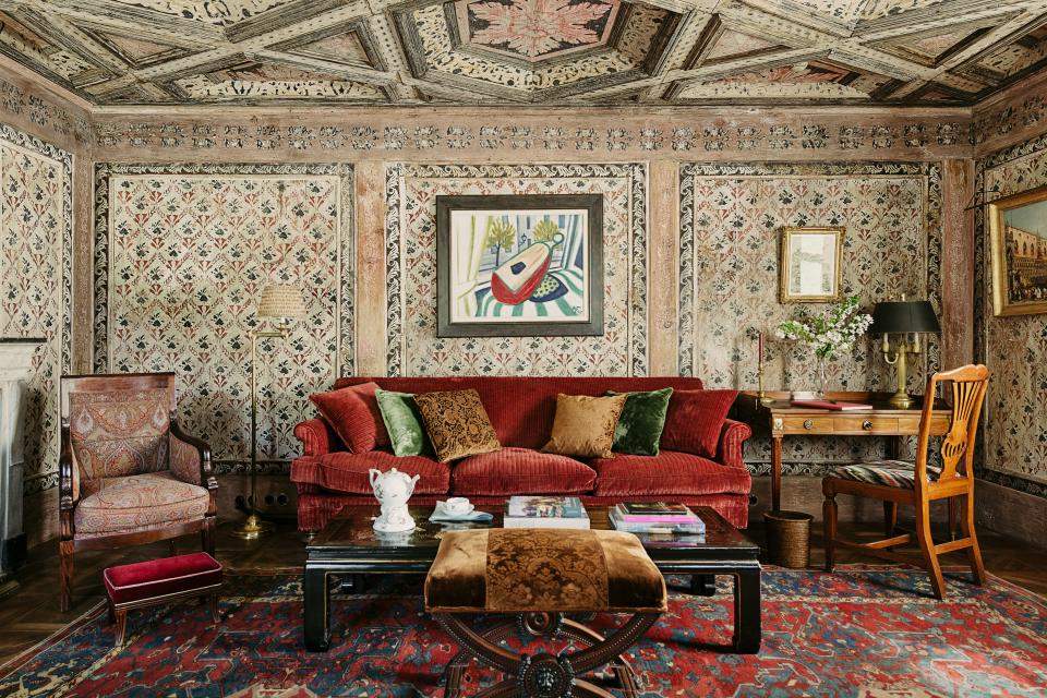 The living room walls and ceiling are covered with wooden Tyrolean paneling from the 18th century. Werner Heldt painting; custom sofa by Studio Peregalli in a red silk velvet; antique Chinese low table.