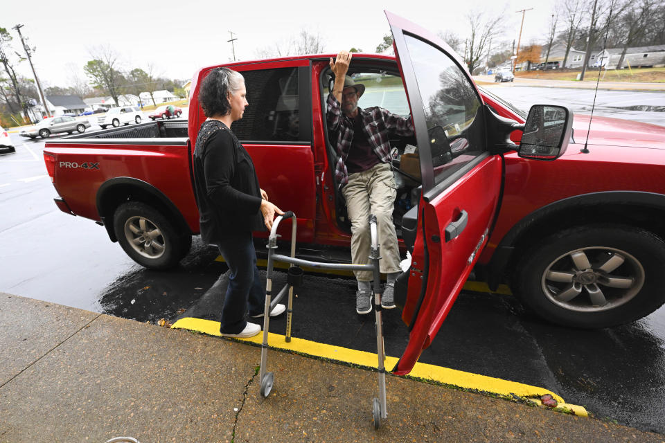 Jerry Lamb, who suffers from a spine condition, gets out of his truck while his wife, Laura, waits to assist him as they arrive at Camden First United Methodist Church Thursday, Dec. 8, 2022, in Camden, Tenn. The church recently had a couple pews cut in half so Jerry, and anyone else who uses a wheelchair, walker or other aid, can still sit with the rest of the congregation. (AP Photo/John Amis)