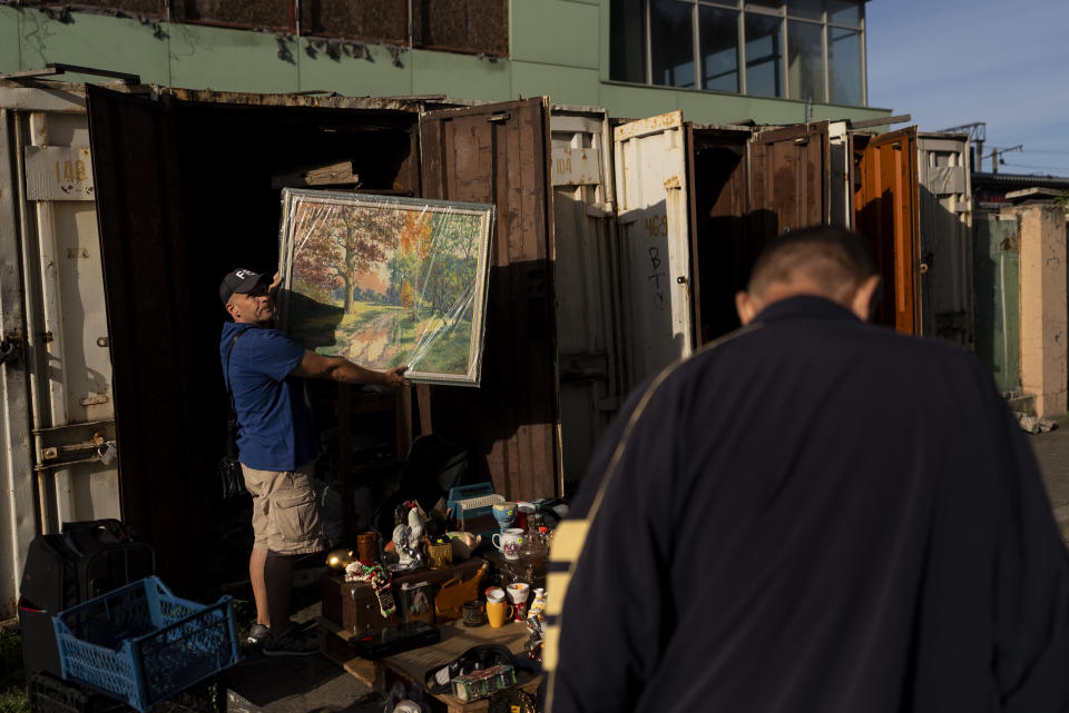 Pavel Sheludko muestra uno de los cuadros que vende a un comprador en un mercado callejero en Kiev, Ucrania, el 9 de julio de 2023. El vecindario de Pochaina de la capital ucraniana cobra vida cada fin de semana cuando cientos de personas acuden en masa a su famoso mercadillo en busca de tesoros. (AP Foto/Jae C. Hong)