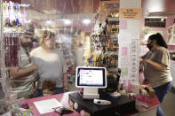 In this Thursday, May 28, 2020, photo, Brandon and Sasha Johnson, and their son Thomas, of Vancouver, Wash., left, through a plastic protective shield check out at Bruce's Candy Kitchen during the coronavirus outbreak in Cannon Beach, Ore. With summer looming, Cannon Beach and thousands of other small, tourist-dependent towns nationwide are struggling to balance fears of contagion with their economic survival in what could be a make-or-break summer. (AP Photo/Gillian Flaccus)