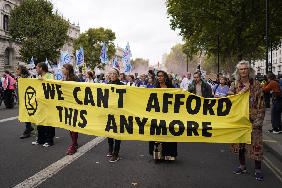 FILE - Extinction Rebellion protesters hold up a banner as they march along Whitehall while others let off flares as they demonstrate near Downing Street in London on Oct. 14, 2022. The U.K. division of climate change protest group Extinction Rebellion says its activists would temporarily stop blocking busy roads, gluing themselves to buildings and engaging in other acts of civil disobedience because such methods have not achieved their desired effects. (AP Photo/Alberto Pezalli, File)