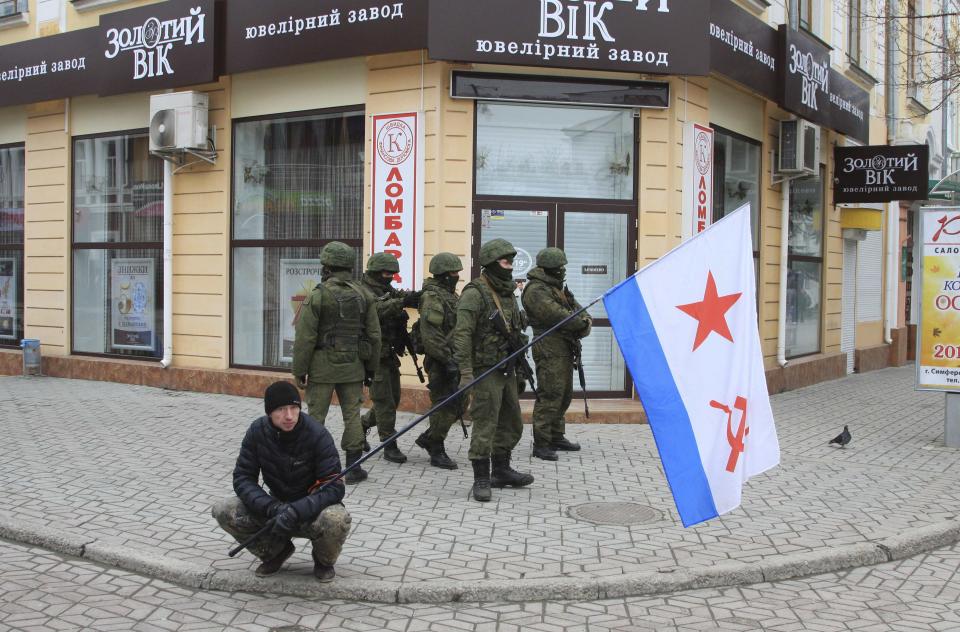 Armed men patrol as a man holds a Soviet Navy flag in the centre of the Crimean city of Simferopol