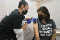 Denise Padilla, right, an instructor at the culinary school at Eva's Village, is vaccinated in Secacus, N.J., Sunday, Feb. 28, 2021. In an effort to vaccinate undeserved populations, Riverside Medical Group partnered with Eva's Village, an anti-poverty non-profit, to help vaccinate over 80 of their clients and staff members. (AP Photo/Seth Wenig)