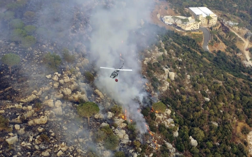 In this frame grab from video, an army helicopter drops water on a fire at the scene of forest fire in Ras el-Harf village, in the Baabda district, Lebanon, Friday, Oct. 9, 2020. Wildfires around the Middle East triggered by a heatwave hitting the region have killed two people, forced thousands of people to leave their homes and detonated landmines along the Lebanon-Israel border, state media and officials said Saturday. (AP Photo)