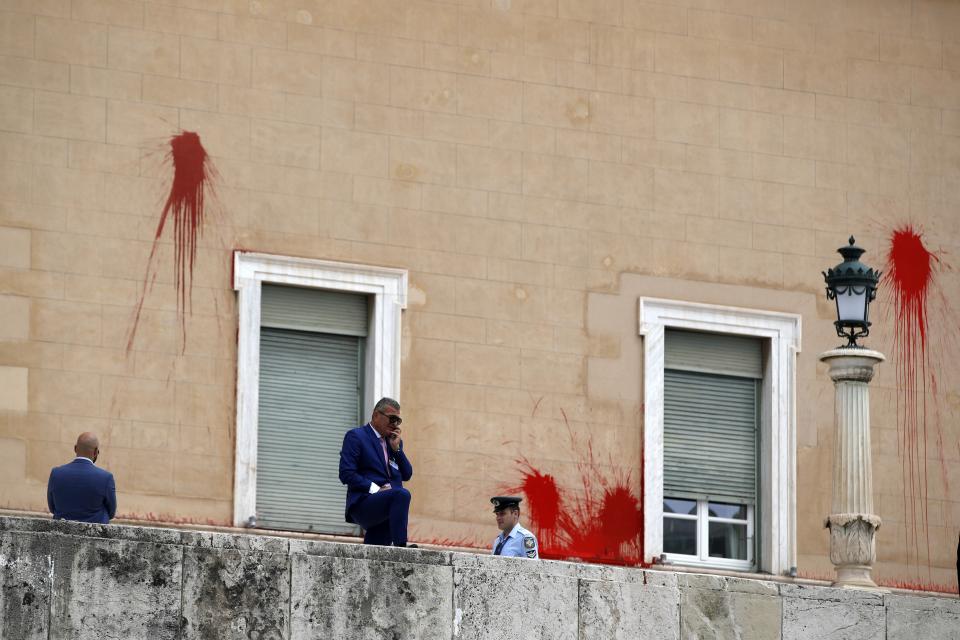 Policemen stand in front of the Parliament building as red paint is seen on the wall in Athens, Tuesday, May 21, 2019. A group of about 10 people threw red paint at parliament and set off a smoke bomb as Greece's Supreme Court heard an appeal against the denial of a temporary leave of absence from prison of a hunger striking extremist serving multiple life sentences for the killings of 11 people by the country's deadliest far-left group. (AP Photo/Thanassis Stavrakis)