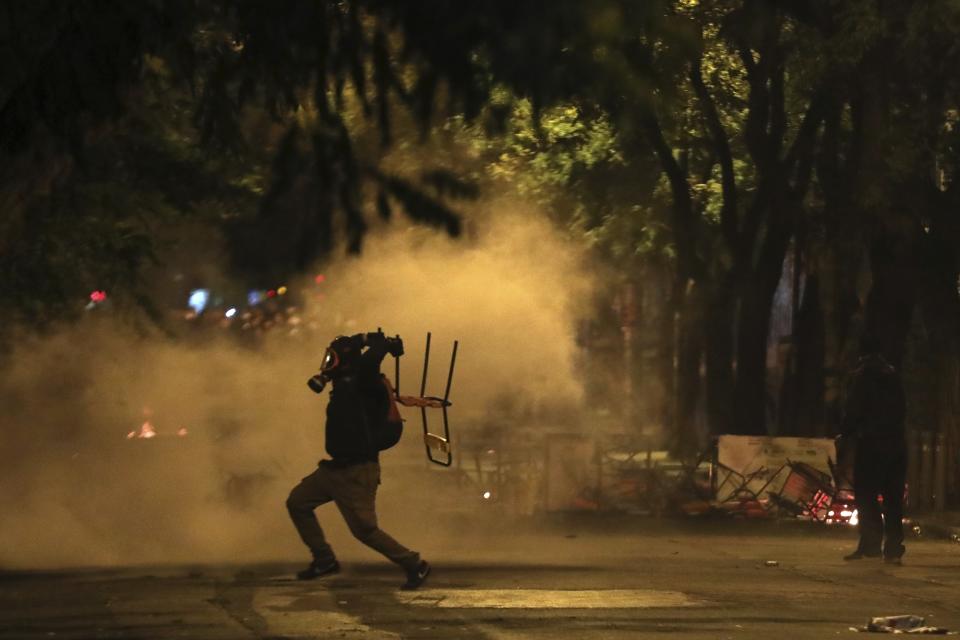 A protester throws a chair at riot police during clashes in the Athens neighborhood of Exarchia, a haven for extreme leftists and anarchists, Saturday, Nov. 17, 2018. Clashes have broken out between police and anarchists in central Athens on the 45th anniversary of a student uprising against Greece's then-ruling military regime. (AP Photo/Yorgos Karahalis)