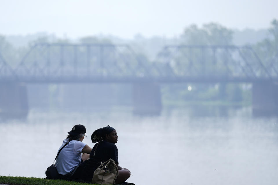 People sit on the banks of the Susquehanna River in haze from Canadian wildfires, Thursday, June 29, 2023, in Harrisburg, Pa. (AP Photo/Matt Rourke)