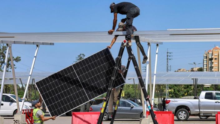 Werknemers installeren nieuwe zonnepanelen om voertuigen te beschermen tegen de zon in de parkeergarage van een winkelcentrum in de stad Byblos, Noord-Libanon, 26 augustus 2022