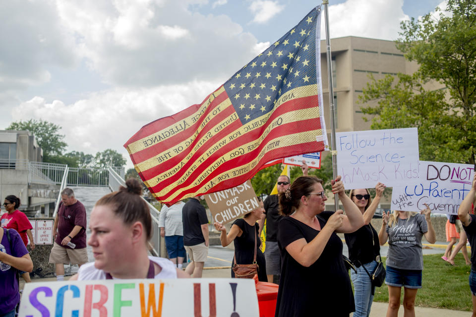 Linden resident Elizabeth Armstrong waves an American flag as she joins hundreds of Genesee County residents protesting against a mandatory mask mandate in schools on Wednesday, Aug. 18, 2021, outside of the Genesee County Administration Building in Flint, Mich.. The Genesee County Health Department instituted a mask mandate for K-6 students school last week. (Jake May/The Flint Journal via AP)