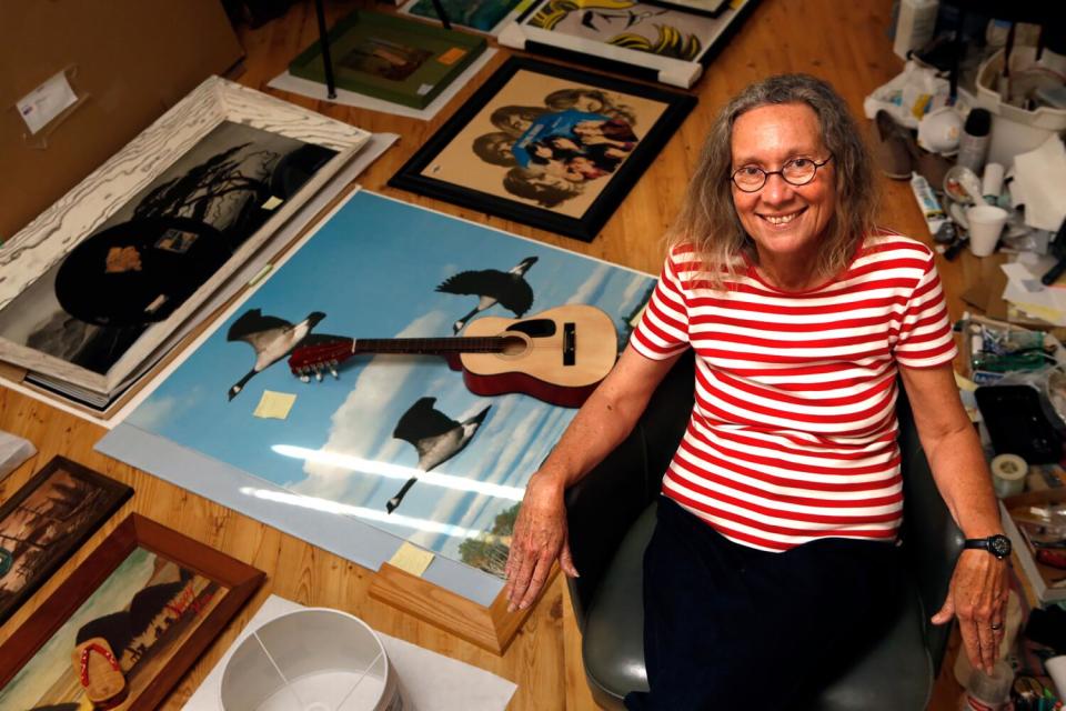 Alexis Smith, in a red and white striped shirt and black pants, is surrounded by her work and supplies in her studio.