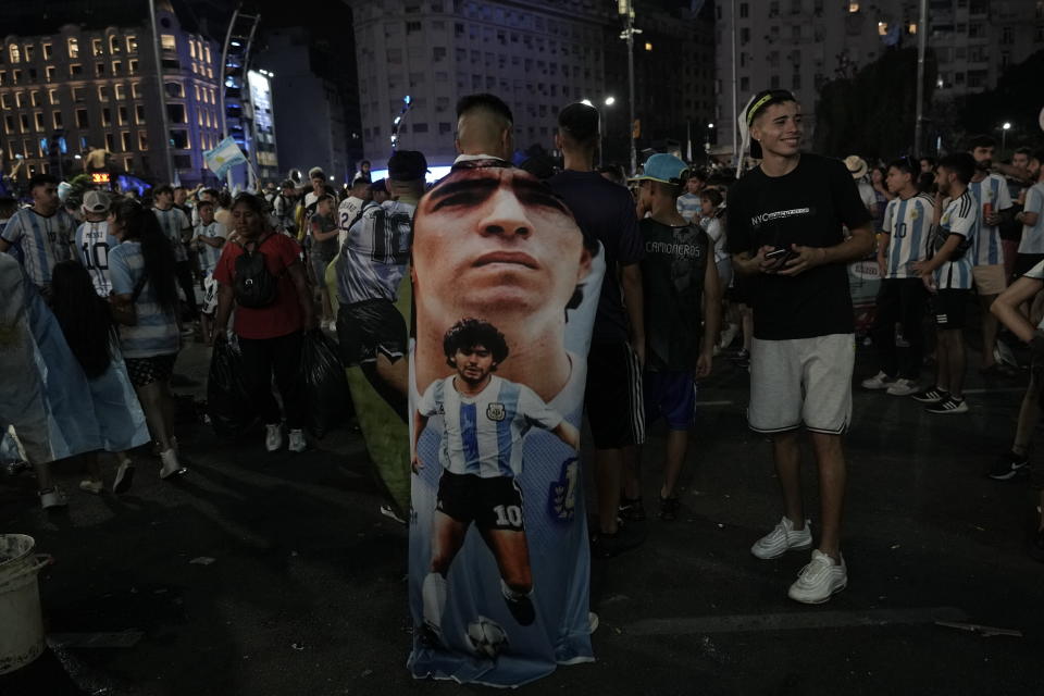 An Argentina soccer fan wears a banner with the image the late soccer star Diego Armando Maradona, during the celebration after the team defeated Croatia in the semifinal World Cup match, in downtown Buenos Aires, Argentina, Tuesday, Dec. 13, 2022. (AP Photo/Rodrigo Abd)