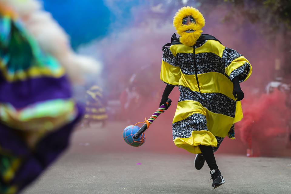 A member of a “bate-bola” or ball hitters group - men who dress up in exuberant, identical, hand-made costumes known as “fantasias” - runs past during a brief appearance as part of a Carnival tradition despite restrictions due to the new coronavirus pandemic, in Rio de Janeiro, Brazil, Saturday, Feb. 13, 2021. Rio’s city government officially suspended Carnival and warns it will have no tolerance for those who try to celebrate with open street parades or clandestine parties. (AP Photo/Bruna Prado)