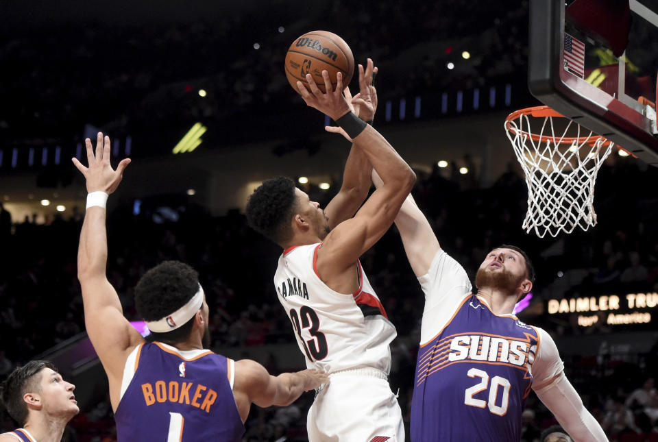 Portland Trail Blazers forward Toumani Camara drives to the basket against Phoenix Suns guard Devin Booker, left, and center Jusuf Nurkic, right, during the second half of an NBA basketball game in Portland, Ore., Tuesday, Dec. 19, 2023. The Blazers won 109-104. (AP Photo/Steve Dykes)