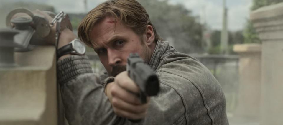 Six holding a gun while handcuffed to a bench in "The Gray Man"