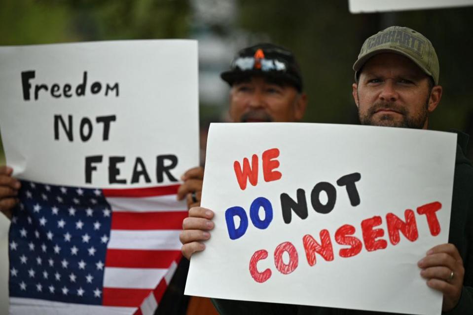 Two men hold protest signs and an American flag. One reads 