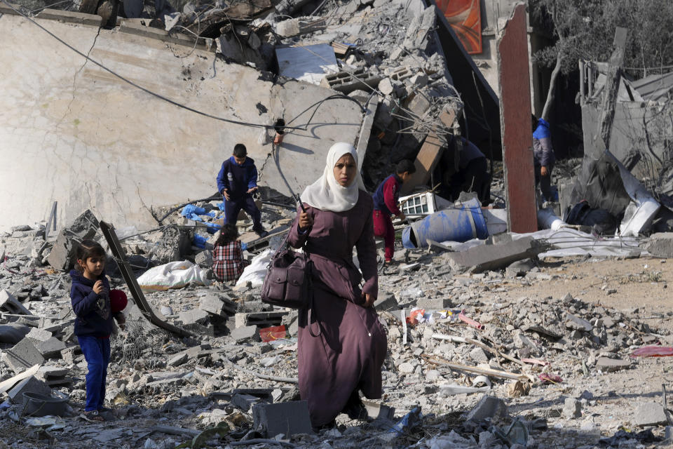 Palestinians walk by the rubble of a building of the Hamad family destroyed in an Israeli strike in Deir al Balah, Gaza Strip, Friday, Dec. 29, 2023. (AP Photo/Adel Hana)