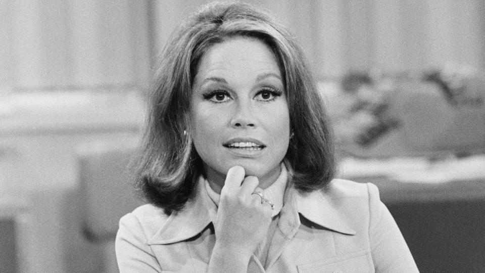 Mary Tyler Moore (as Mary Richards) sits at her desk, hand on her chin, and looks thoughtful in a scene from "The Mary Tyler Moore Show."
