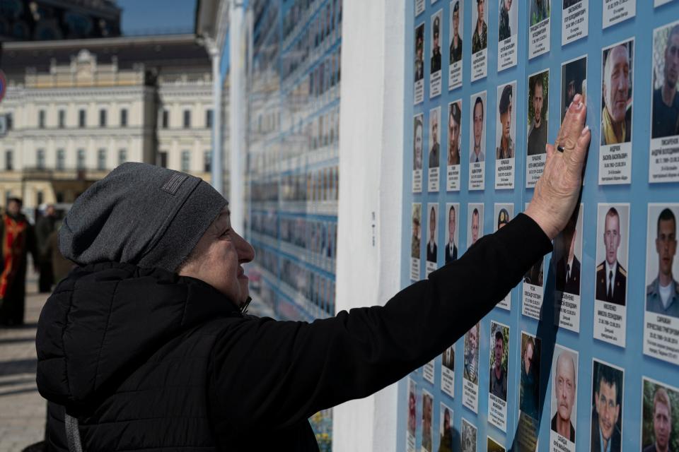 A woman touches a picture as she stands next to the Memory Wall of Fallen Defenders of Ukraine in Russian-Ukrainian War on Ukrainian Volunteer Day in Kyiv, Ukraine, Tuesday, March 14, 2023.