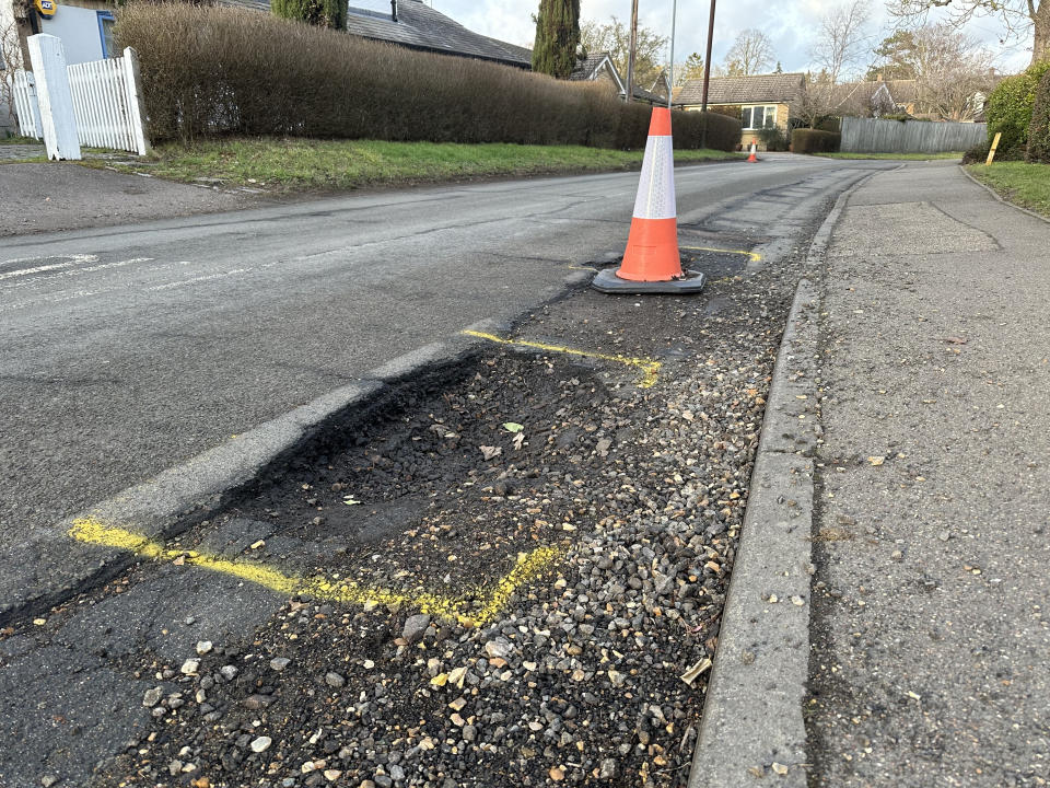 Badly damaged road with pot holes and traffic come to warn motorists