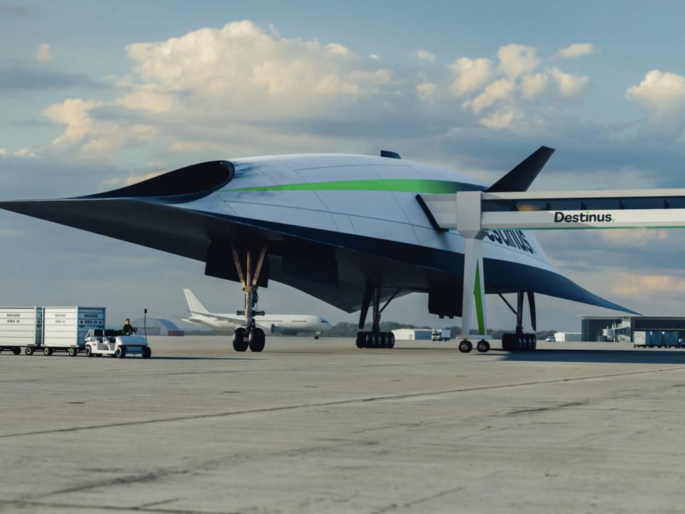 A concept image of the Destinus L, a sleek-looking vehicle with its landing gear down, parked at an airport with the passenger bridge extended.