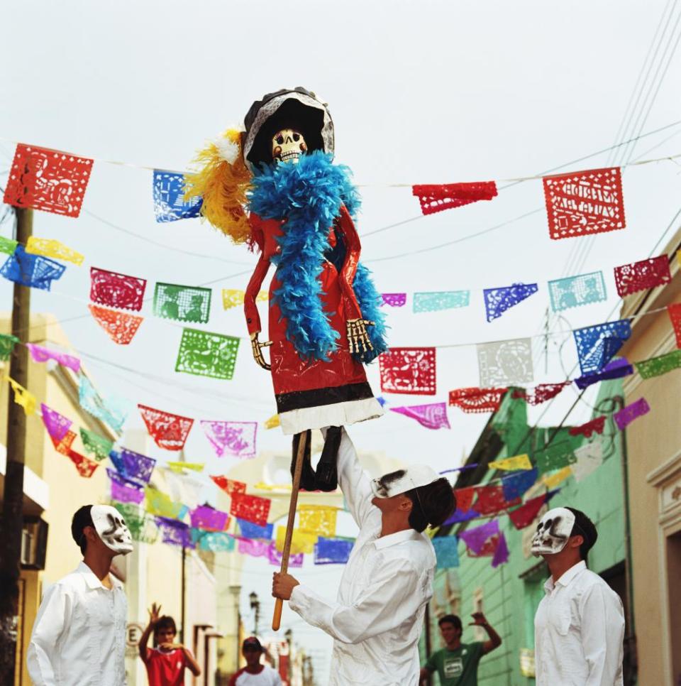 Three men wearing skeleton masks looking up at Day of the Dead puppetMerida, Baja California Norte, Mexico