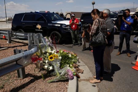 People look at flowers placed at the site of a mass shooting where 20 people lost their lives at a Walmart in El Paso