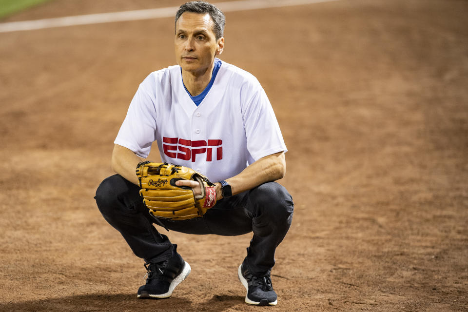 ESPN President Jimmy Pitaro squats with his hand in a baseball glove on a baseball field.