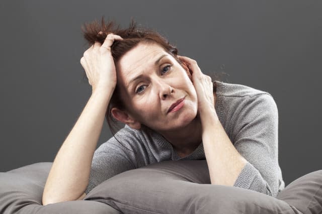 tired senior woman resting her face and hands laying down on cushions for comfort and relaxation