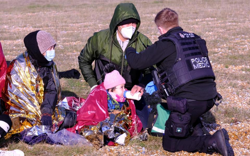 Police speak to migrants feeding one of their children after a group landed on the beach at Dungeness on Wednesday