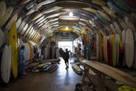 Surf shop worker Francois wears a mask as he carries a surfboard as Bird's Surf Shed opens Friday, May 8, 2020, in San Diego. California Gov. Gavin Newsom on Thursday issued the broadest loosening of his stay-at-home order so far, allowing retailers and manufacturers to reopen with new safety measures and setting strict criteria. (AP Photo/Gregory Bull)