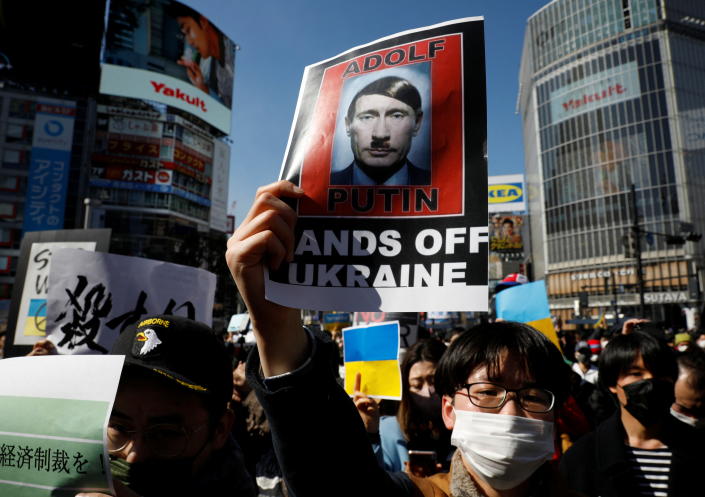 A protester in a white mask holds up a poster saying: 