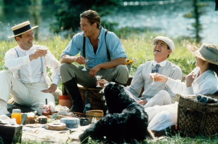Three men and one woman sit down and have a picnic.