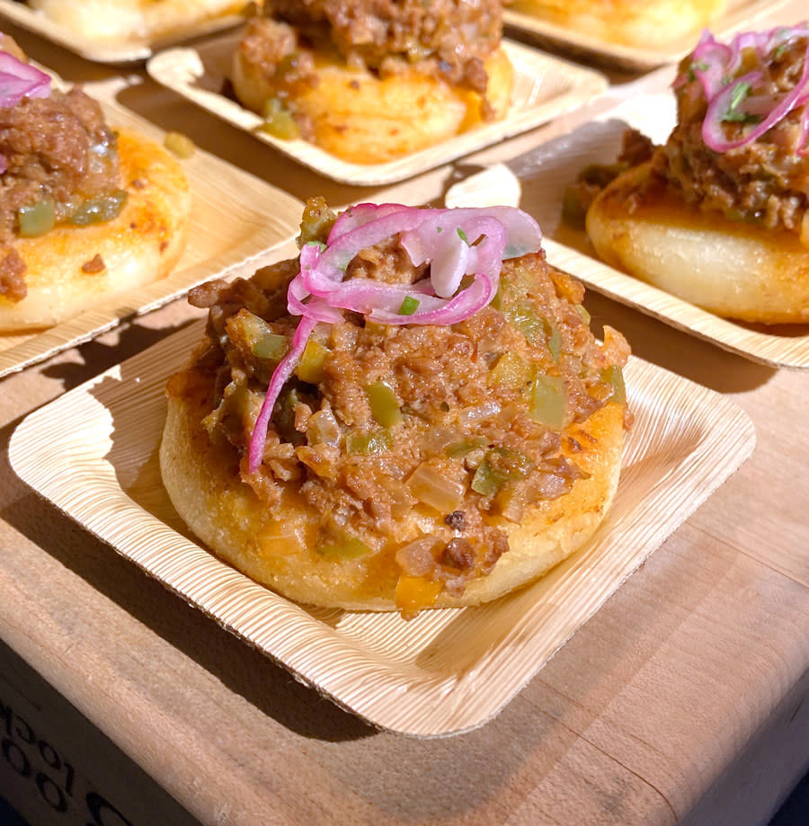 A small arepa encantada topped with impossible meat, queso, and pickled onion