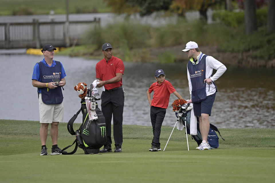 Tiger Woods, second from left, and his son Charlie wait to hit from the 18th fairway as caddies Joe LaCava, left, and Joe LaCava Jr., right, watch during the final round of the PNC Championship golf tournament, Sunday, Dec. 20, 2020, in Orlando, Fla. (AP Photo/Phelan M. Ebenhack)