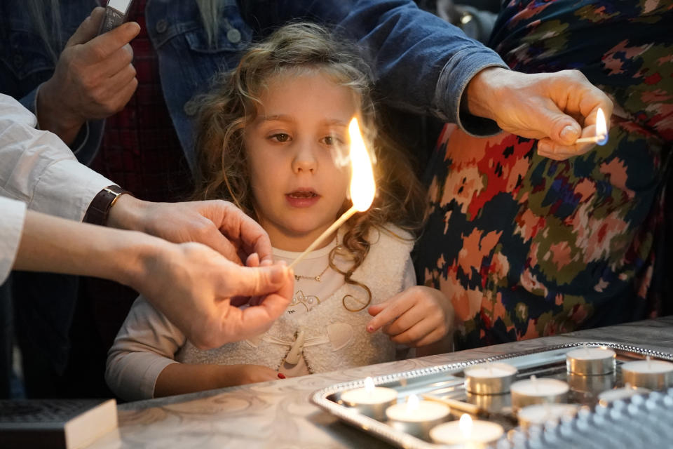 Maayan Hilel's daughter Emilia, watches as her mother lights candles to mark the beginning of Shabbat on Friday, Oct. 20, 2023, in Evanston, Ill. Judith Raanan, a member of Chabad, and her daughter Natalie were released Friday from their captivity in Gaza. (AP Photo/Charles Rex Arbogast)