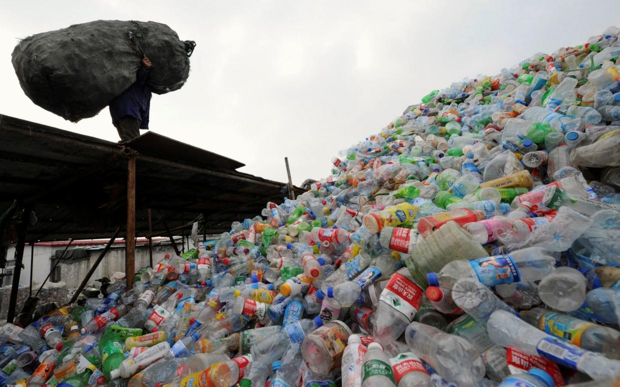 A man carries a bag of plastic bottles on a roof at a recycling centre in Hefei - Jianan Yu /Reuters