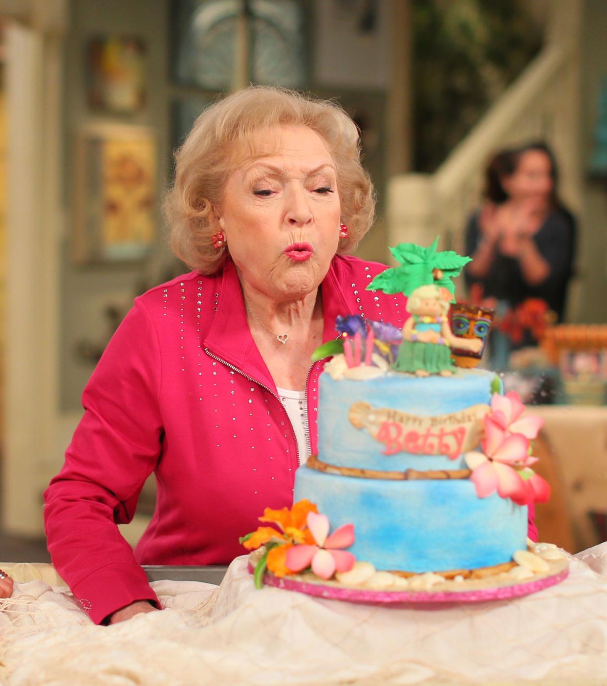 Betty White blows out a Hawaiian themed cake that says "Happy Birthday Betty"